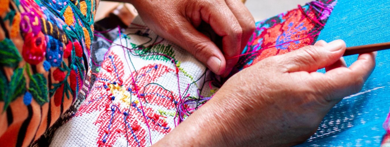 **En el corazón de Centroamérica**, ***Guatemala*** tiene las tradiciones más ricas y vibrantes del mundo: la herencia textil maya. Antigua, una ciudad envuelta en el misticismo de las ruinas coloniales y rodeada por volcanes imponentes, junto con las diversas comunidades a lo largo de Guatemala, continúa siendo el epicentro de esta tradición milenaria. Esta [Aventura por la cultura maya y sus textiles](https://dev.travelisimo.com/es/guatemala/actividades/tours-y-experiencias/antigua-guatemala/tour-de-textiles-antigua?adult=2&currency=USD&country=GT&) se adentra en el mundo de los textiles mayas, explorando sus orígenes, significados, y la manera en que estas prácticas ancestrales continúan influyendo en la moda y textiles contemporáneos.

![Textiles Guatemala](https://cdn.travelisimo.com/1_042c886844)

---

El algodón, junto con el hilo de agave, constituye la base de los textiles mayas. La introducción del telar de cintura revolucionó la producción textil, permitiendo la creación de diseños complejos y coloridos. Cada pieza refleja la maestría y la dedicación de sus creadores, siendo un testimonio de su profundo respeto por la naturaleza y sus recursos.

![Hilo y Algodon](https://cdn.travelisimo.com/2_ac97f9b11a)

---

Los textiles mayas están imbuidos de simbolismo. Los colores, patrones, y figuras no son elecciones aleatorias; representan elementos de la cosmología maya, como el sol, la luna, la tierra, y el maíz. Estos textiles son una forma de comunicación no verbal, una manera de expresar identidad, estatus social, y afiliaciones comunitarias.

![Textiles](https://cdn.travelisimo.com/5_1a98267668)

---

Lejos de ser prácticas del pasado, las técnicas y estilos de los textiles mayas continúan influyendo en la moda contemporánea. Diseñadores tanto locales como internacionales se inspiran en la riqueza de estos textiles, incorporándose en colecciones que trascienden fronteras, fusionando tradición y modernidad.
 
![Locales](https://cdn.travelisimo.com/6_670d9fcda8)
---

A pesar de su importancia cultural y estética, los textiles mayas enfrentan amenazas por la globalización y la producción en masa. Sin embargo, los esfuerzos de conservación y programas de sustentabilidad buscan preservar estas prácticas, asegurando que la herencia textil maya perdure para futuras generaciones.

![Textiles](https://cdn.travelisimo.com/4_36f9f4dda8)
