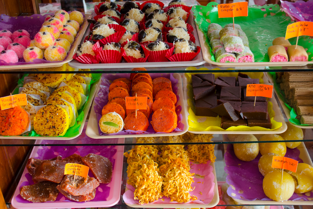 Los Dulces Típicos son los dulces coloridos y tradicionales de Guatemala. Normalmente disfrutados durante las vacaciones como Semana Santa y Fiestas de los Santos, estas delicias se remontan a la época colonial y son ricas en tradición e historia. Los dulces en sí varían mucho debido a la diversidad de frutas, semillas y edulcorantes naturales que se encuentran en Guatemala. Estos son algunos de nuestros favoritos:

## Bolitas de Tamarindo 
Hechas de tamarindo enrollado en una bolita y luego cubiertas con azúcar, son una delicia agridulce. ¡Tenga cuidado, a menudo encontrará semillas de tamarindo adentro!

## Canillitas de Leche
Llamadas así por su forma larga y delgada y hechas de leche, azúcar y canela, las canillitas son, con mucho, uno de los dulces tradicionales más populares entre niños y adultos por igual.

## Colochos de Guayaba
Un dulce tradicional que se consume durante las fiestas de los santos patrones, este dulce masticable está hecho de guayaba, azúcar y especias y lleva el nombre de su forma única de rizo.

## Higos en Dulce
Los higos fueron traídos originalmente a Guatemala por los españoles en la época colonial. Aquí se confitan con azúcar y especias y se sirven en su propio almíbar.

## Chilacayote
Un trozo de calabaza confitado con almíbar y especias, este dulce de textura y sabor únicos se puede comer frío o caliente.

## Mazapán
Hecho de almendras crudas y azúcar triturado en una pasta suave y tersa, el mazapán o mazapán, como se lo conoce en inglés, se moldea y se sirve en una variedad de formas tradicionales, la mayoría de las cuales son frutas.

Antigua es particularmente famosa por sus dulces típicos y los guatemaltecos siempre se aseguran de abastecerse de sus favoritos en las tiendas locales cuando visitan la ciudad colonial. Estos dulces también se venden a veces frente a las iglesias y por los vendedores ambulantes durante las fiestas y ferias locales.