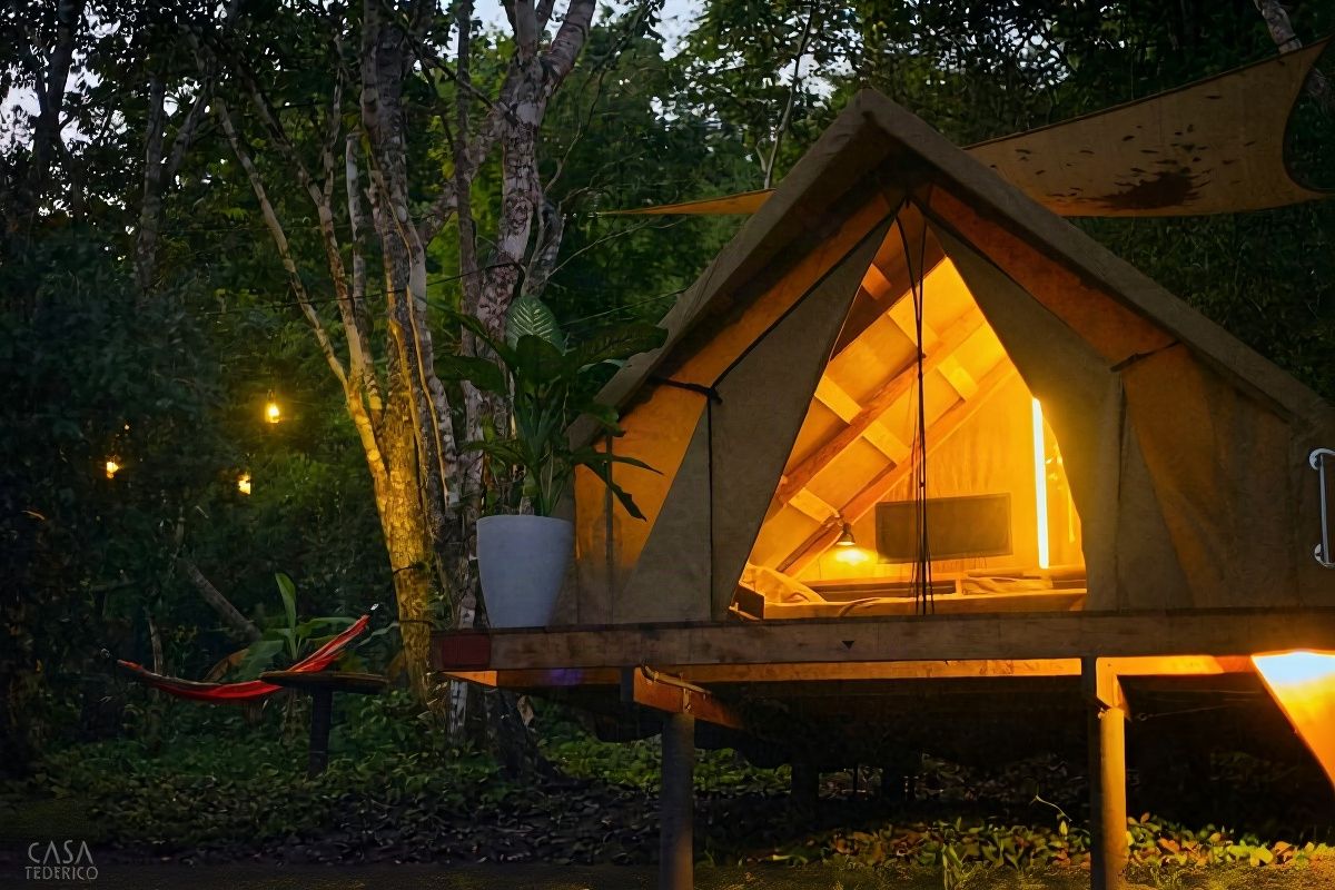 Beige canvas glamping tent elevated in Petén Itzá jungle at sunset, Guatemala, surrounded by tall trees and tropical canopy with red hammock nearby