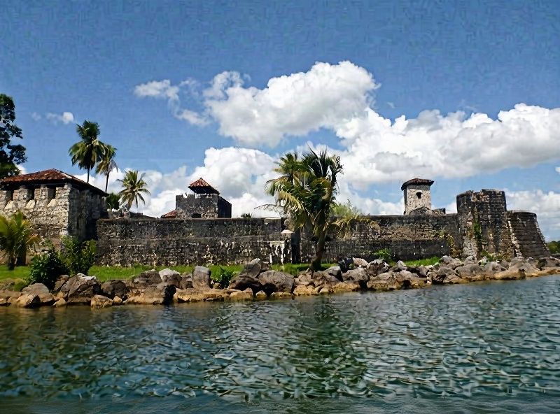 San Felipe de Lara fortress with gray stone walls, cylindrical towers and red-tiled roofs on the Río Dulce in Izabal, Guatemala, surrounded by tropica