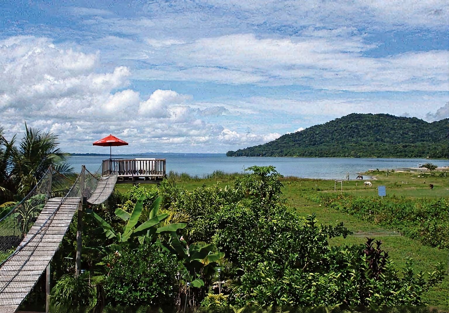 Wooden deck with red umbrella on turquoise waters of Lake Petén Itzá in Guatemala surrounded by Mayan jungle