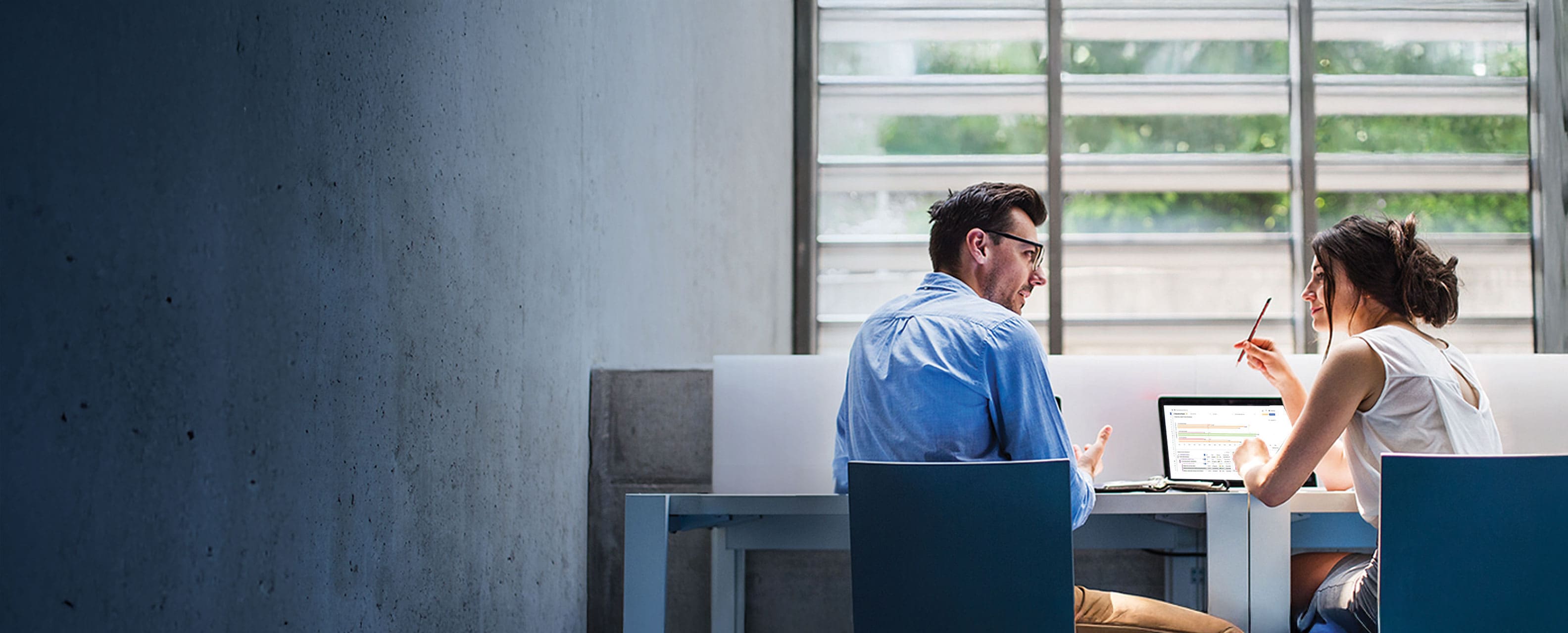 Man and woman speaking to each other as they work on a laptop